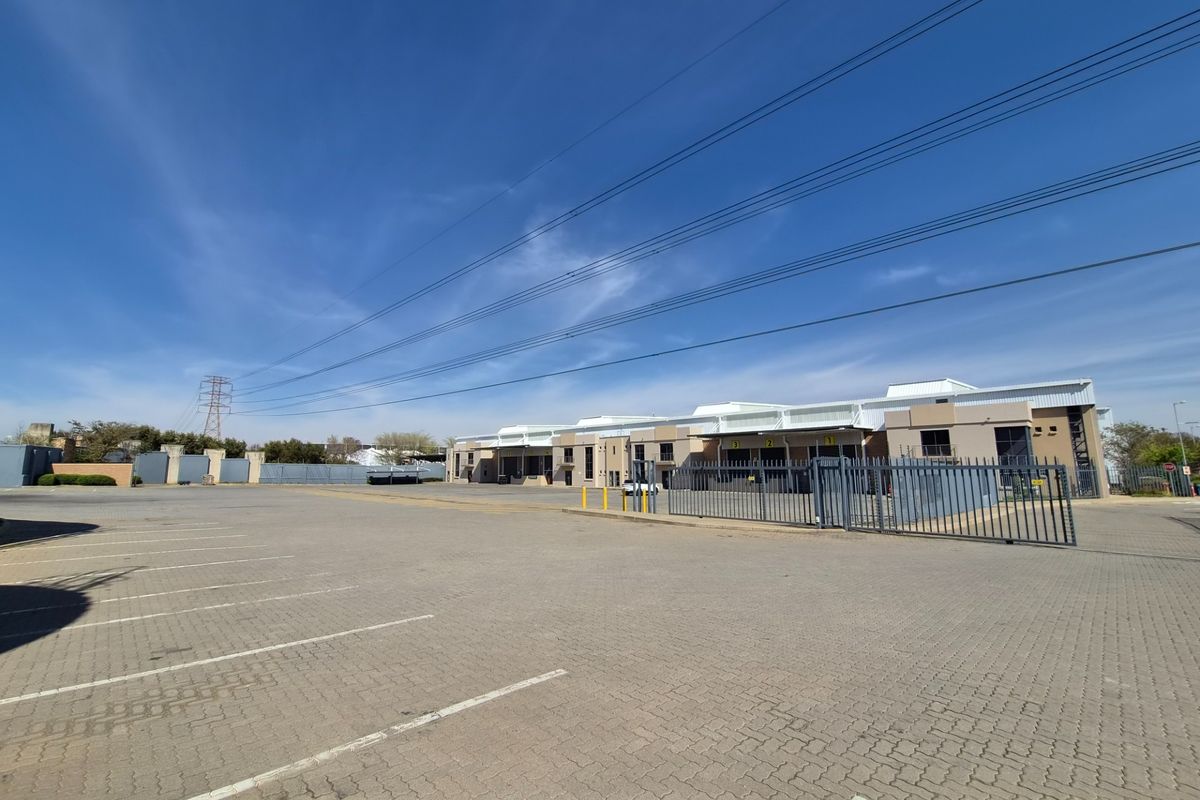 Wide-angle view of an industrial property featuring a large paved parking area, secure metal fencing, and multiple warehouse loading bays.