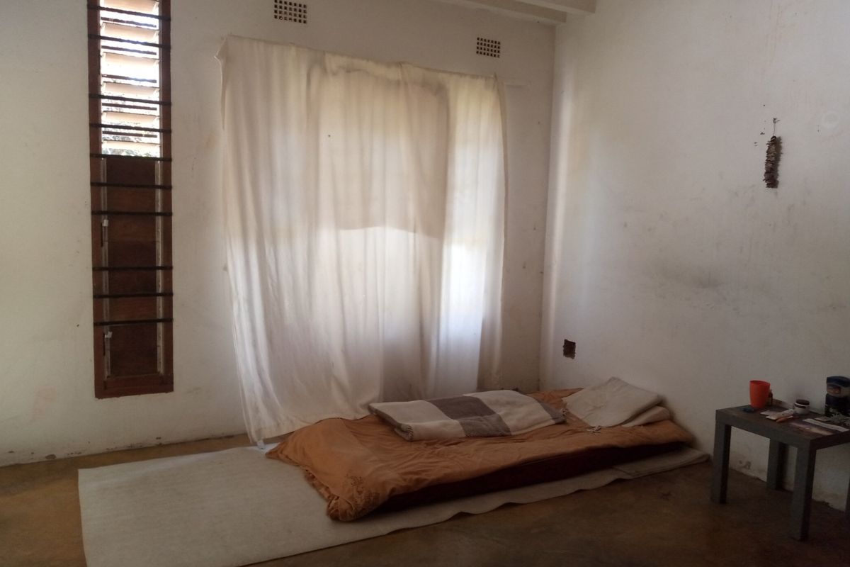 A bedroom featuring concrete flooring, exposed beam ceilings, and louvre windows, requiring cosmetic updates to improve the overall finish and condition.