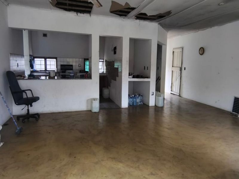 Open plan living and kitchen area featuring concrete flooring and significant ceiling damage, requiring extensive renovation and repair.