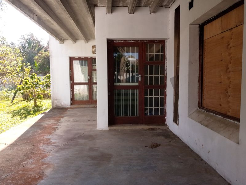 Covered patio area featuring concrete ceiling beams, timber framed glass doors with security bars, and concrete flooring, requiring maintenance and cosmetic updates.