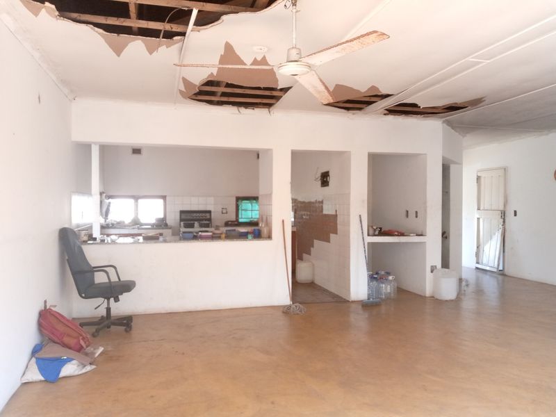 Open plan living and kitchen area featuring a breakfast counter and significant ceiling damage requiring immediate repair and renovation.