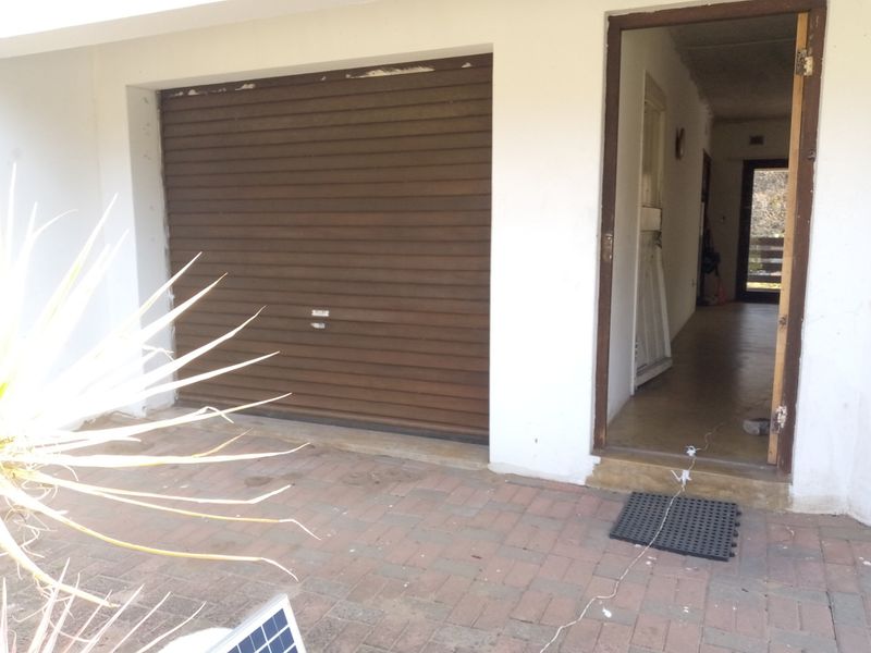 Exterior view of a garage with a roller shutter door and adjacent entrance, featuring paved driveway area and basic structural finishes.