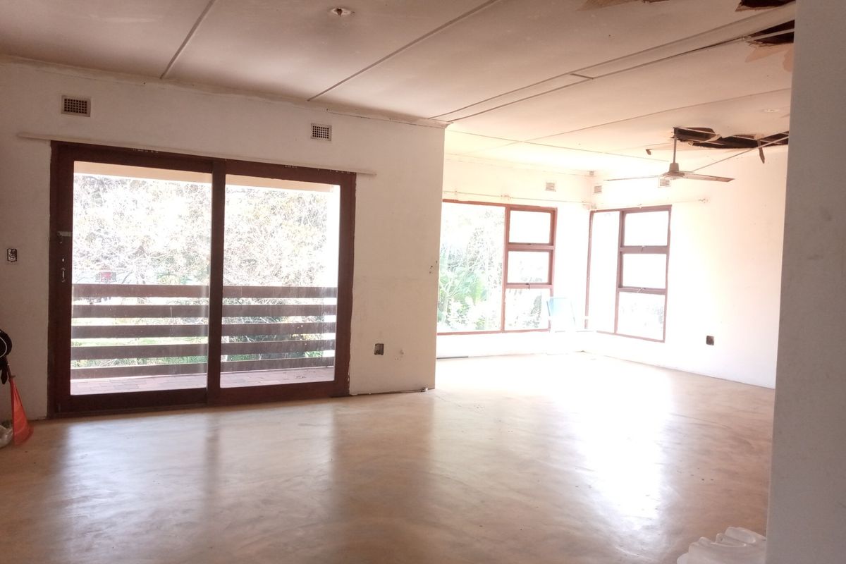 Spacious, empty living area featuring polished concrete floors, large sliding glass doors, and significant ceiling damage requiring repair.