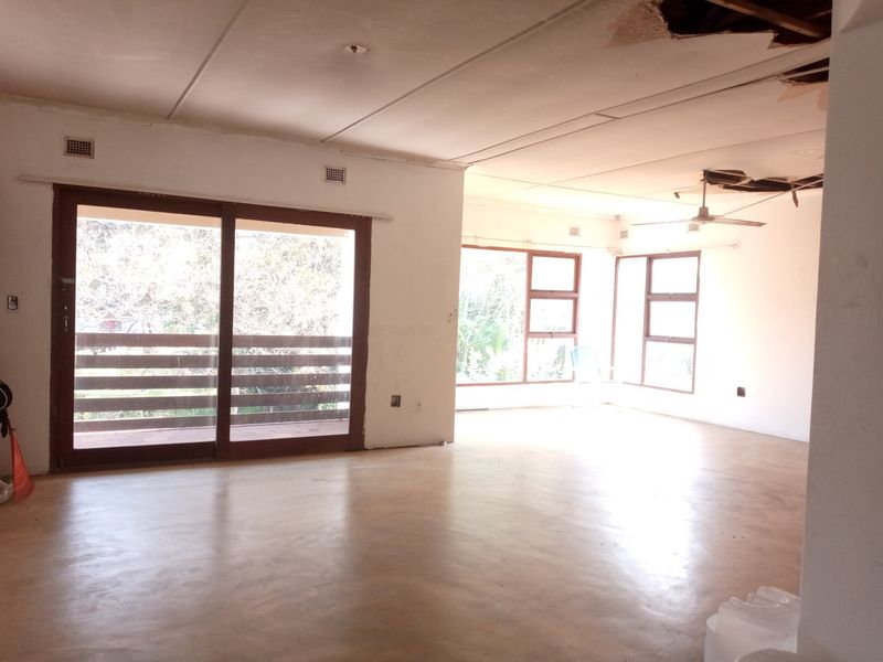 Spacious, empty living area featuring polished concrete floors, large sliding glass doors, and significant ceiling damage requiring repair.