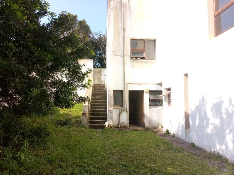 Rear exterior view of the property featuring a concrete staircase leading to an upper level and weathered white exterior walls.