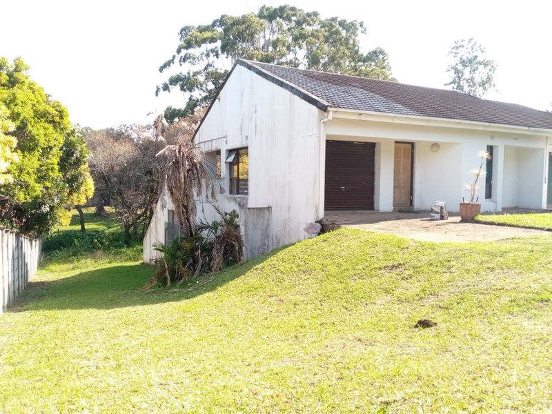 Front exterior view of a single-story house featuring a tiled roof, roller garage door, and concrete driveway, set on a sloped grass lot.