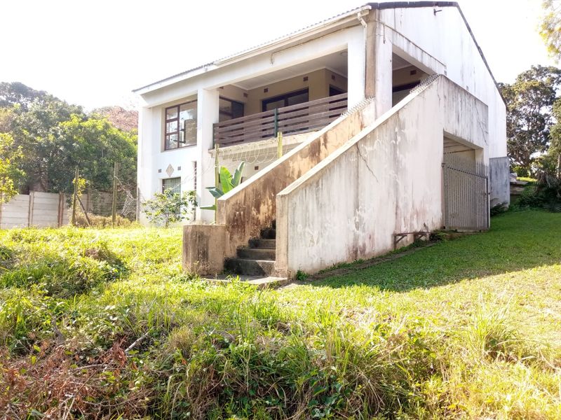 Rear view of a two-story house featuring an elevated balcony, external concrete staircase, and security fencing, requiring significant exterior maintenance and painting.