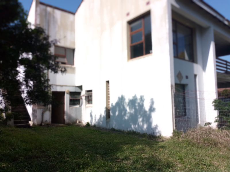 Rear view of a multi-story residential property featuring white exterior walls, aluminium window frames, and a small lawn area.