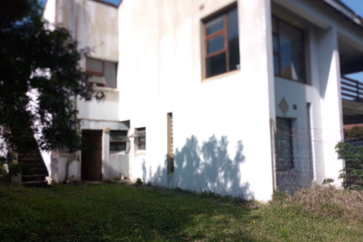 Rear view of a multi-story residential property featuring white exterior walls, aluminium window frames, and a small lawn area.
