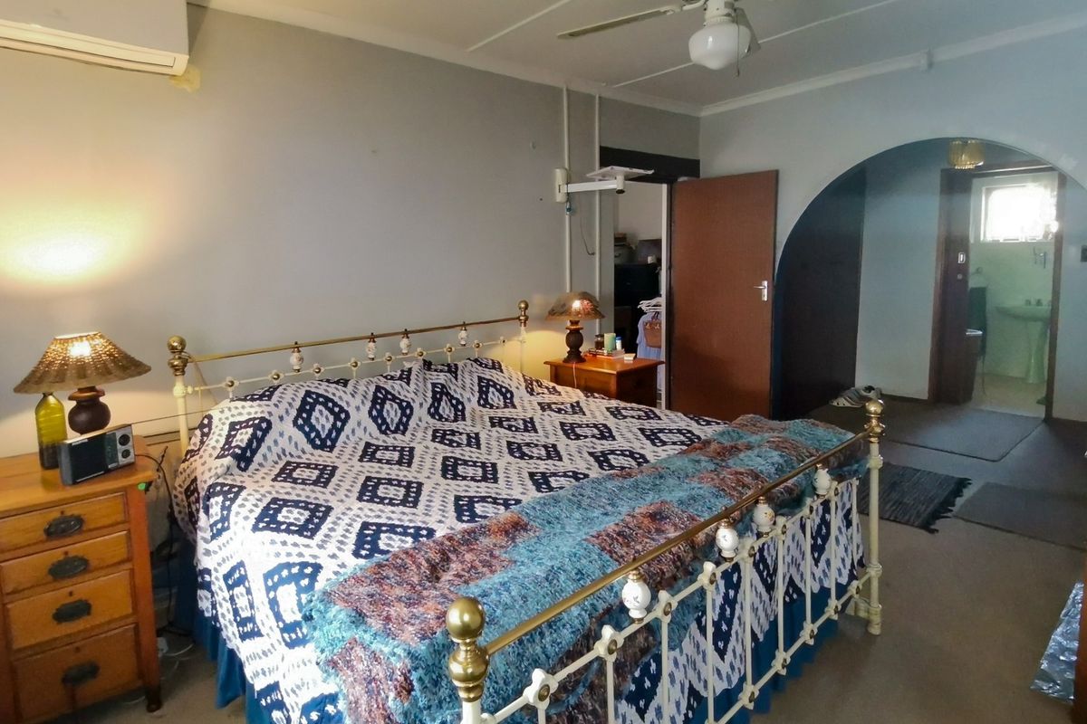 A bedroom featuring a ceiling fan, wall-mounted air conditioner, and an arched doorway leading to an adjacent room.