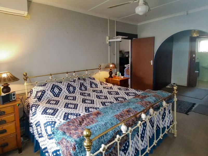 A bedroom featuring a ceiling fan, wall-mounted air conditioner, and an arched doorway leading to an adjacent room.