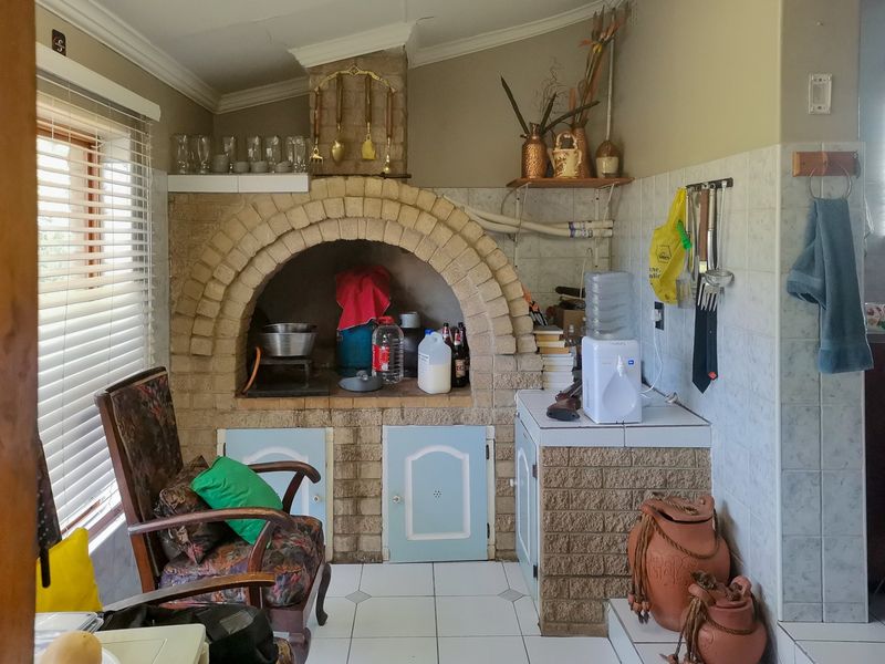 A rustic kitchen area featuring a prominent built-in brick fireplace, tiled flooring, and tiled splashbacks, offering potential for a modern renovation.