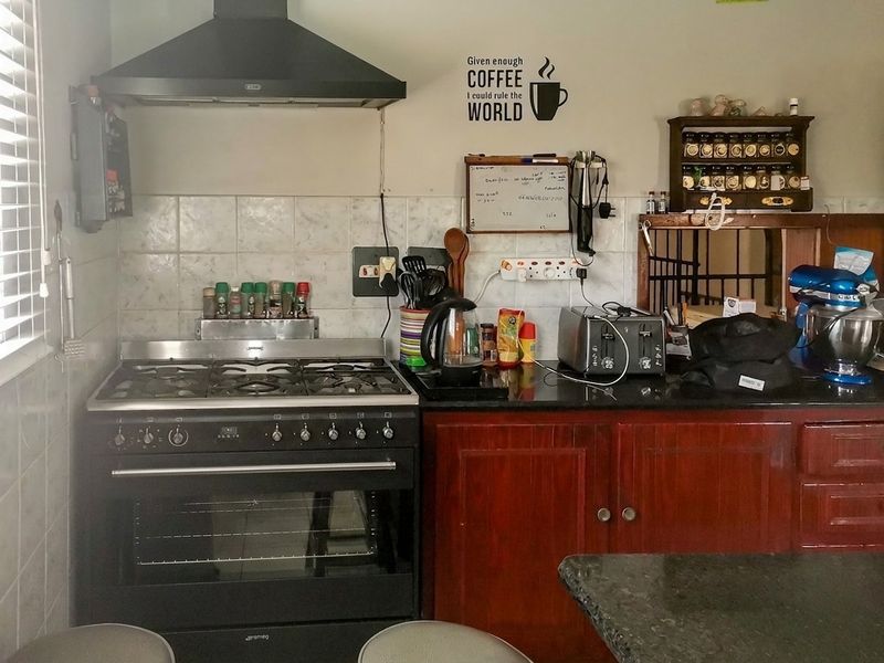 A functional kitchen featuring a gas stove, extractor fan, granite countertops, and wooden cabinetry with a tiled backsplash.