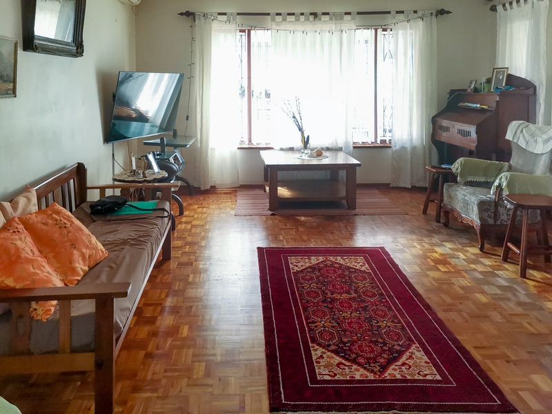 A spacious living room featuring classic parquet flooring and a large window that allows for ample natural light.