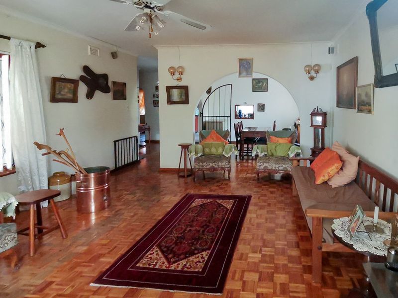 Spacious living room featuring classic parquet flooring, a central ceiling fan, and an elegant archway leading to the dining area.
