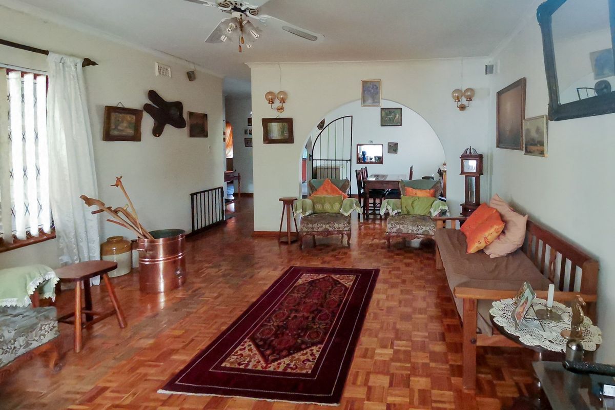 Spacious living room featuring classic parquet flooring, a central ceiling fan, and an elegant archway leading to the dining area.