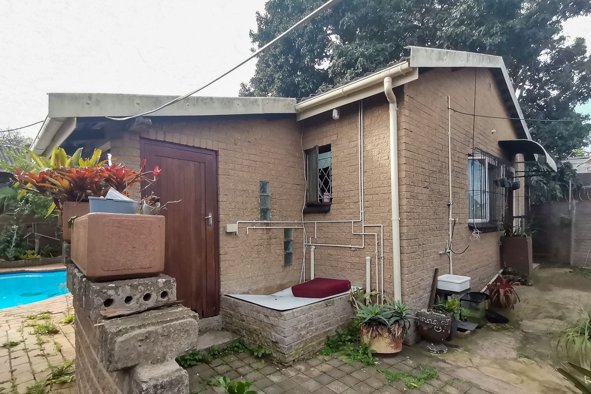 Rear exterior view of the property featuring brick construction, external plumbing, and security bars on windows, adjacent to a pool area.