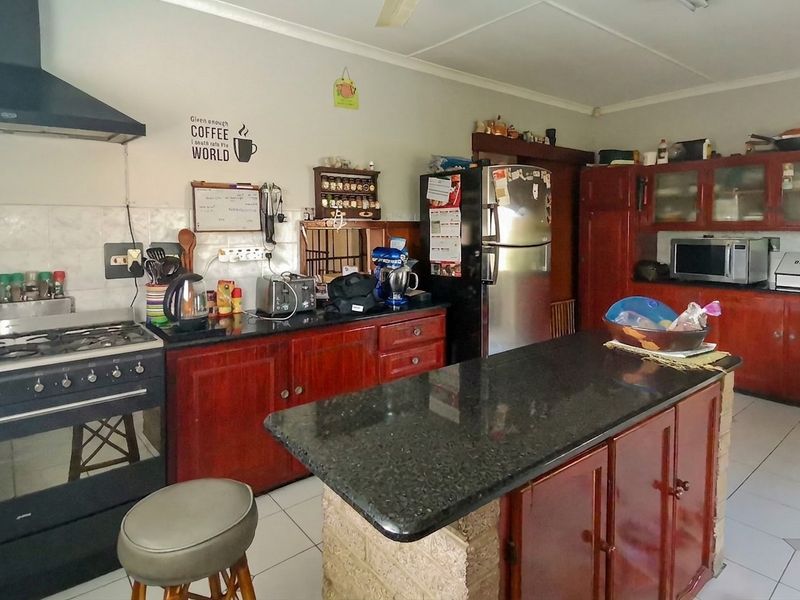 A functional kitchen featuring dark wood cabinetry, granite countertops, a central island with a brick base, and a gas stove with an extractor fan.