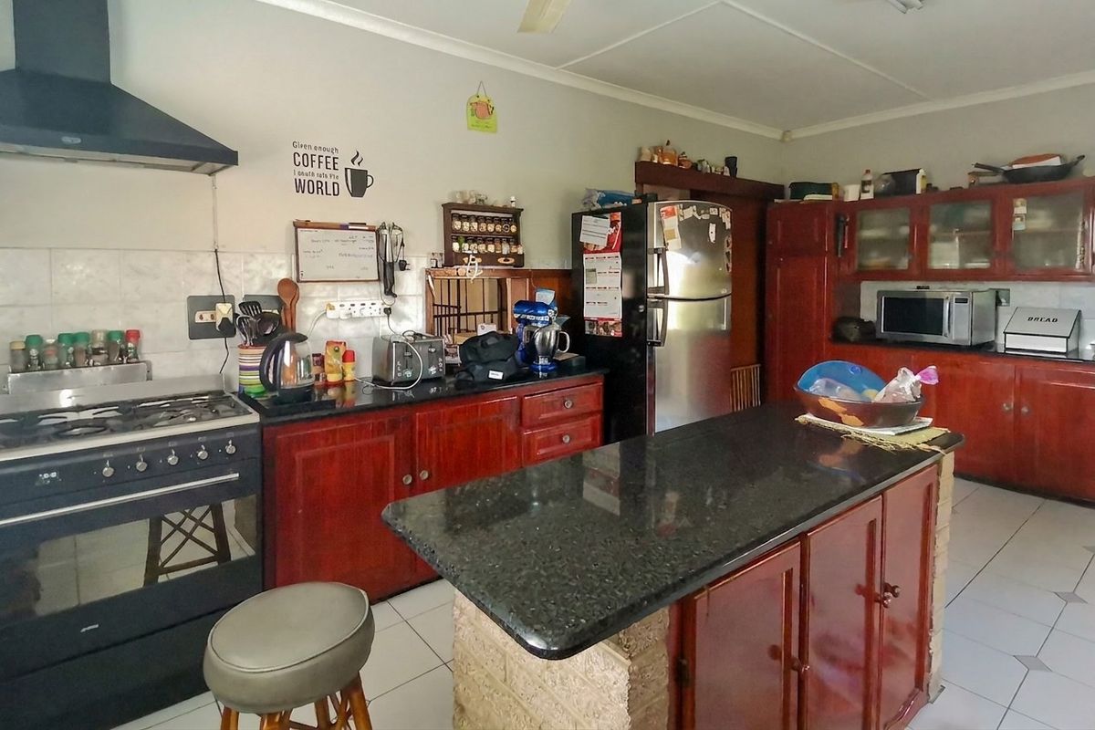 A functional kitchen featuring dark wood cabinetry, granite countertops, a central island with a brick base, and a gas stove with an extractor fan.