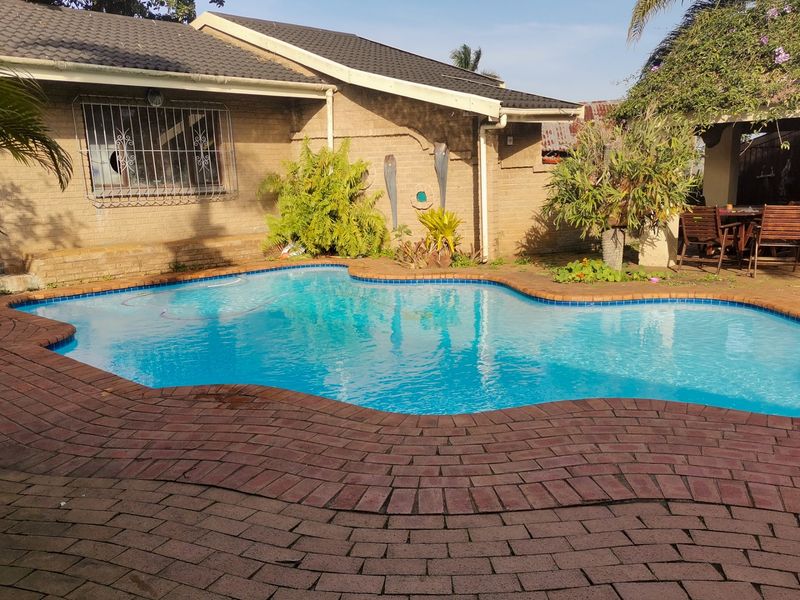 A backyard pool area featuring a swimming pool, brick paving, and a covered patio area adjacent to the main house structure.