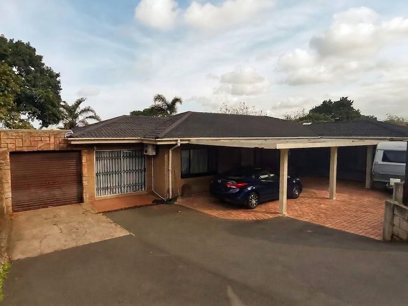 Front exterior view of the house featuring a paved driveway, attached carport, single garage, and brick facade with security gate.