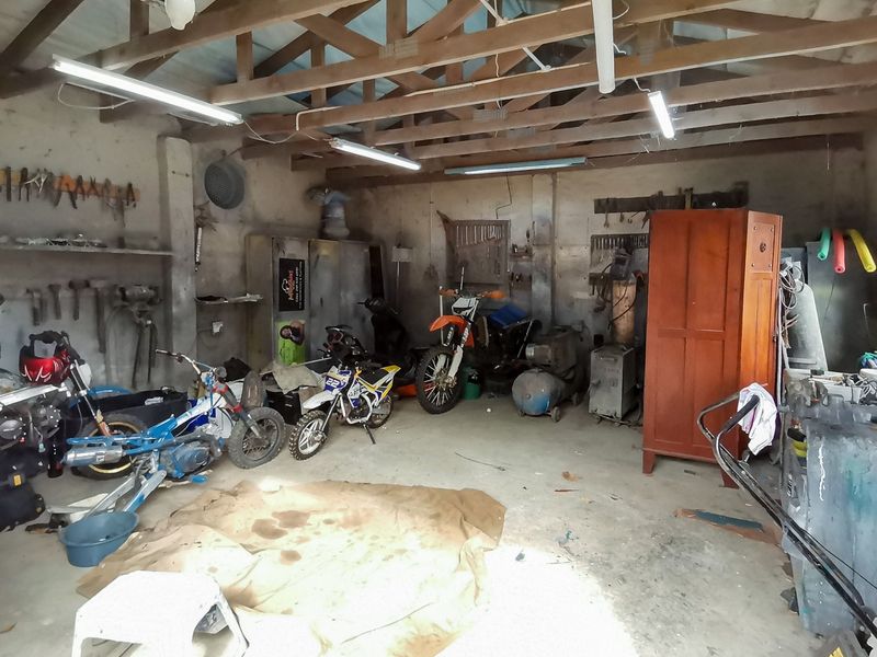 A functional garage space featuring exposed timber roof trusses, concrete flooring, and wall-mounted storage, offering potential for workshop or vehicle storage use.