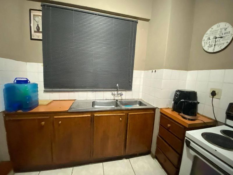 A functional kitchen area featuring wooden cabinetry, a double bowl stainless steel sink, and tiled splashbacks, requiring cosmetic updates to modernize the space.