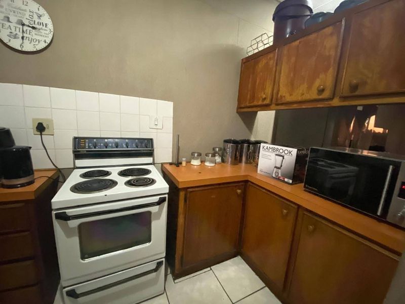 A dated kitchen featuring wooden cabinetry, laminate countertops, and a freestanding electric stove with a tiled splashback.