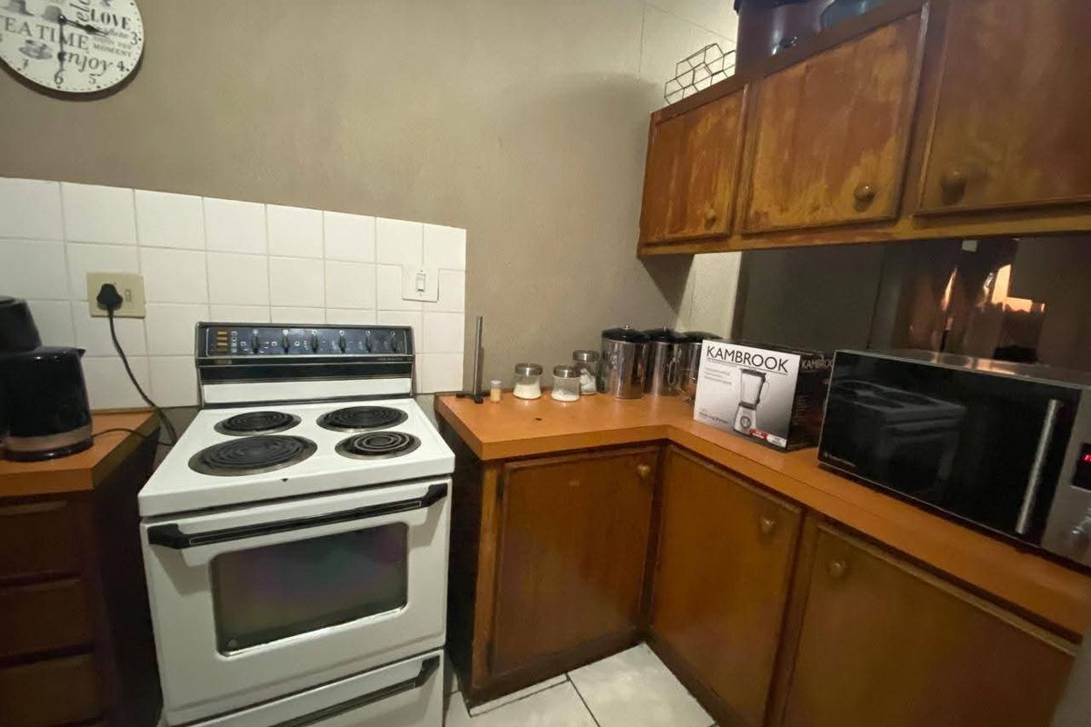 A dated kitchen featuring wooden cabinetry, laminate countertops, and a freestanding electric stove with a tiled splashback.