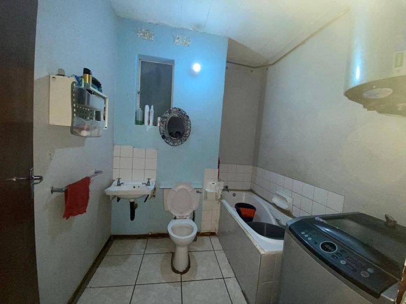 A functional bathroom featuring a wall-mounted basin, toilet, and bathtub with tiled splashbacks, requiring cosmetic updates to improve its overall condition.