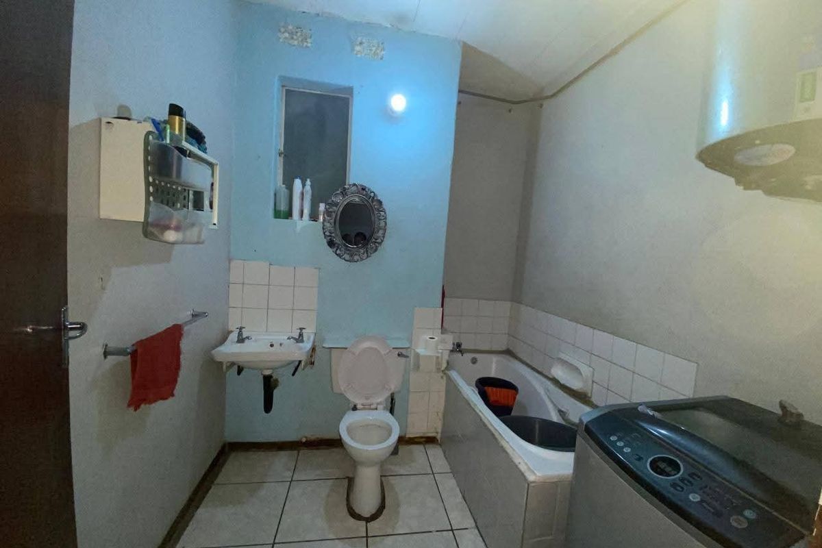 A functional bathroom featuring a wall-mounted basin, toilet, and bathtub with tiled splashbacks, requiring cosmetic updates to improve its overall condition.