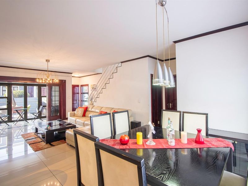 Spacious open-plan living and dining area featuring polished tiled floors, modern pendant lighting, and a staircase, with direct access to an outdoor patio.