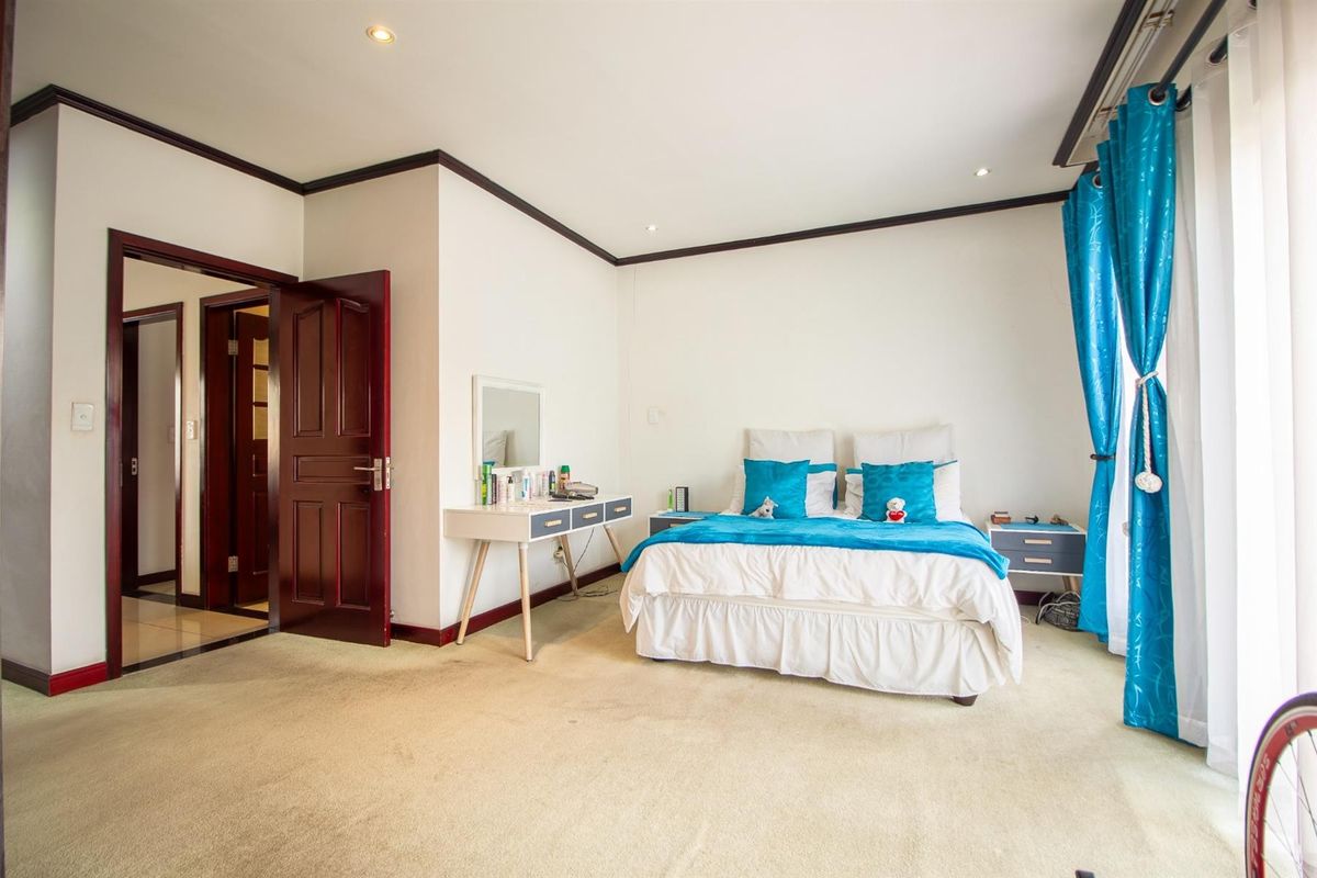 A spacious bedroom featuring neutral carpeting, recessed downlighting, and dark timber door frames, offering a clean and functional living space.