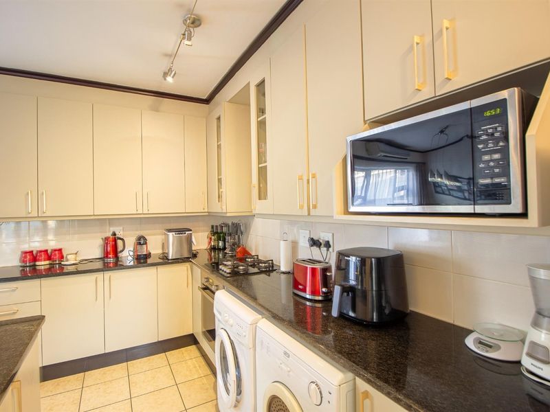 A functional kitchen featuring cream-colored cabinetry, dark granite countertops, a gas hob, built-in oven, and integrated microwave with tiled backsplash and flooring.