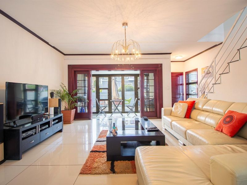 Spacious living room featuring polished porcelain floor tiles, a modern staircase, and large french doors providing access to the outdoor patio area.