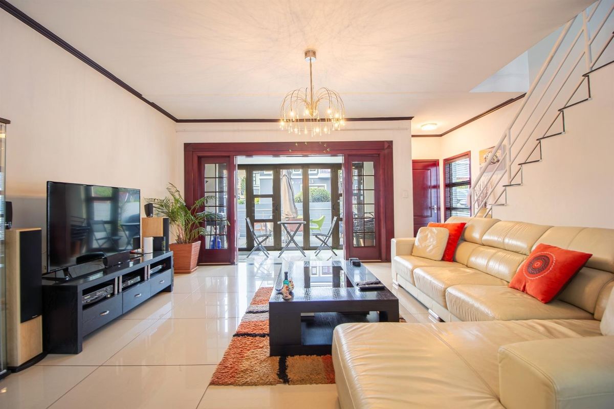 Spacious living room featuring polished porcelain floor tiles, a modern staircase, and large french doors providing access to the outdoor patio area.