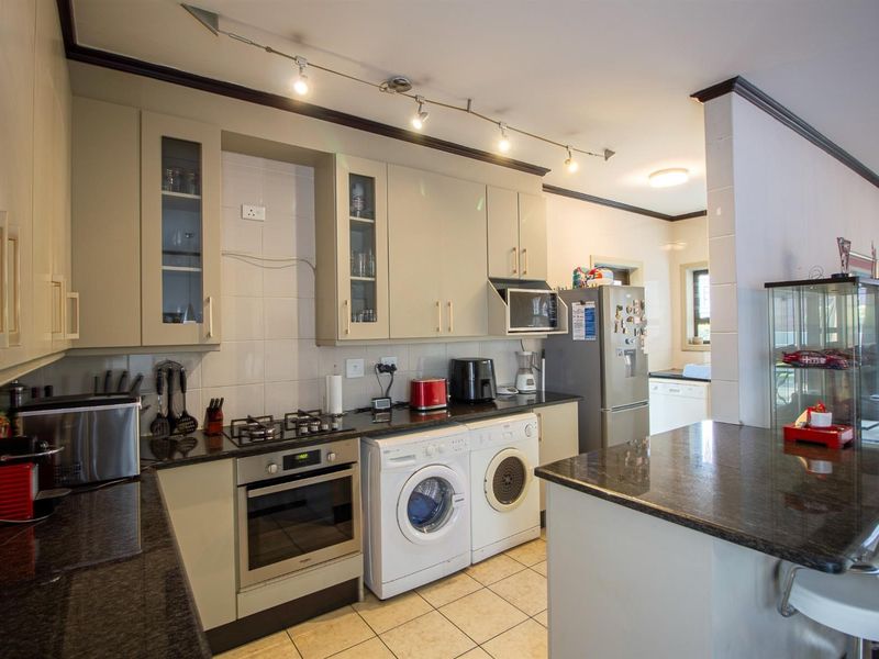 A functional kitchen featuring granite countertops, built-in cabinetry, integrated appliances, and a breakfast bar, with tiled flooring and track lighting.
