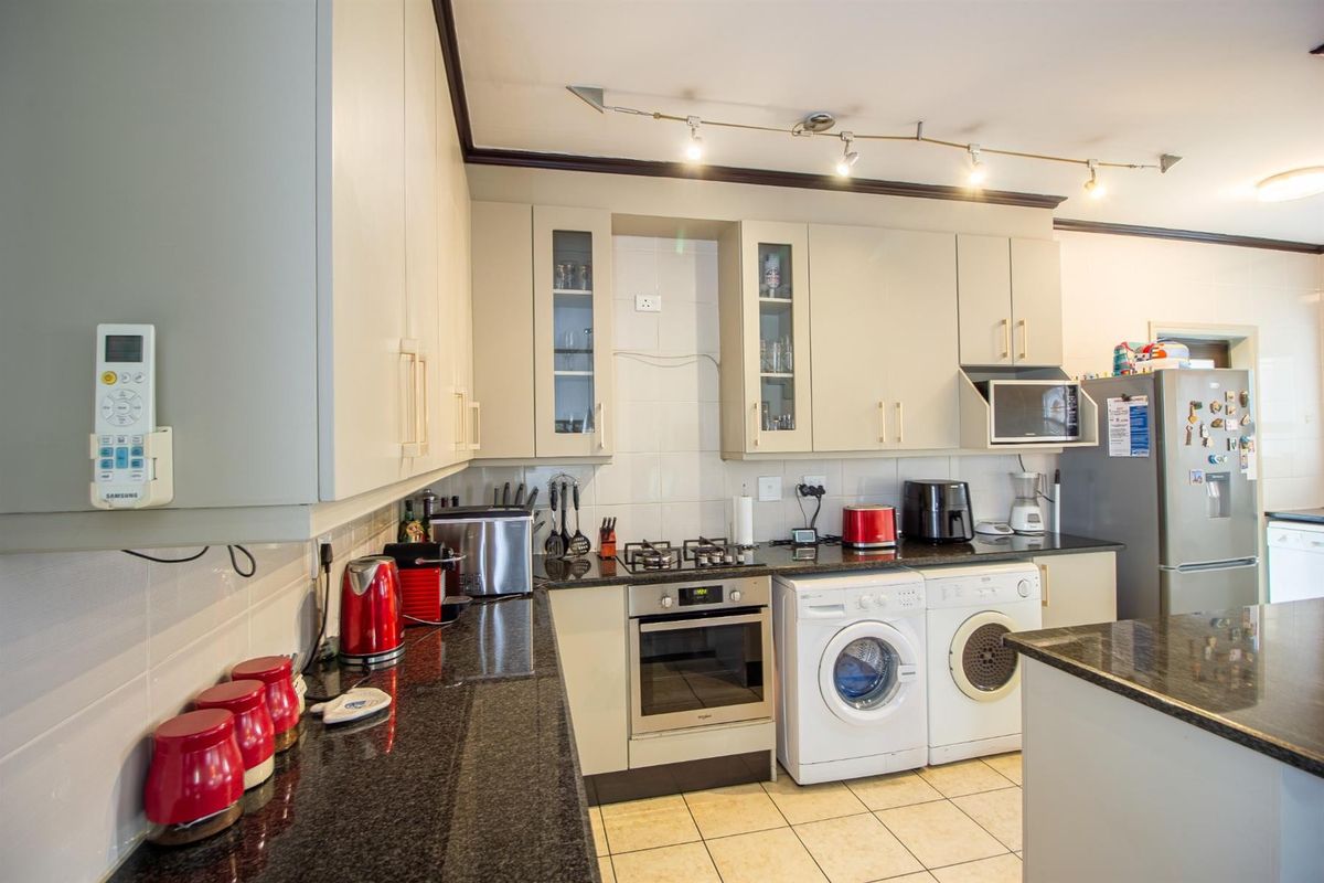 A functional kitchen featuring granite countertops, built-in cabinetry, a gas hob, an integrated oven, and tiled flooring with space for laundry appliances.
