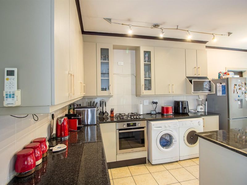A functional kitchen featuring granite countertops, built-in cabinetry, a gas hob, an integrated oven, and tiled flooring with space for laundry appliances.