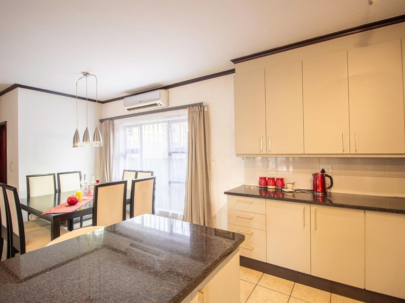 Open-plan kitchen and dining area featuring granite countertops, ample built-in cabinetry, tiled flooring, and a wall-mounted air conditioning unit.