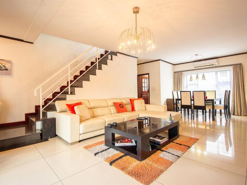 Spacious open-plan living and dining area featuring polished tiled flooring, a central staircase, and modern pendant lighting.