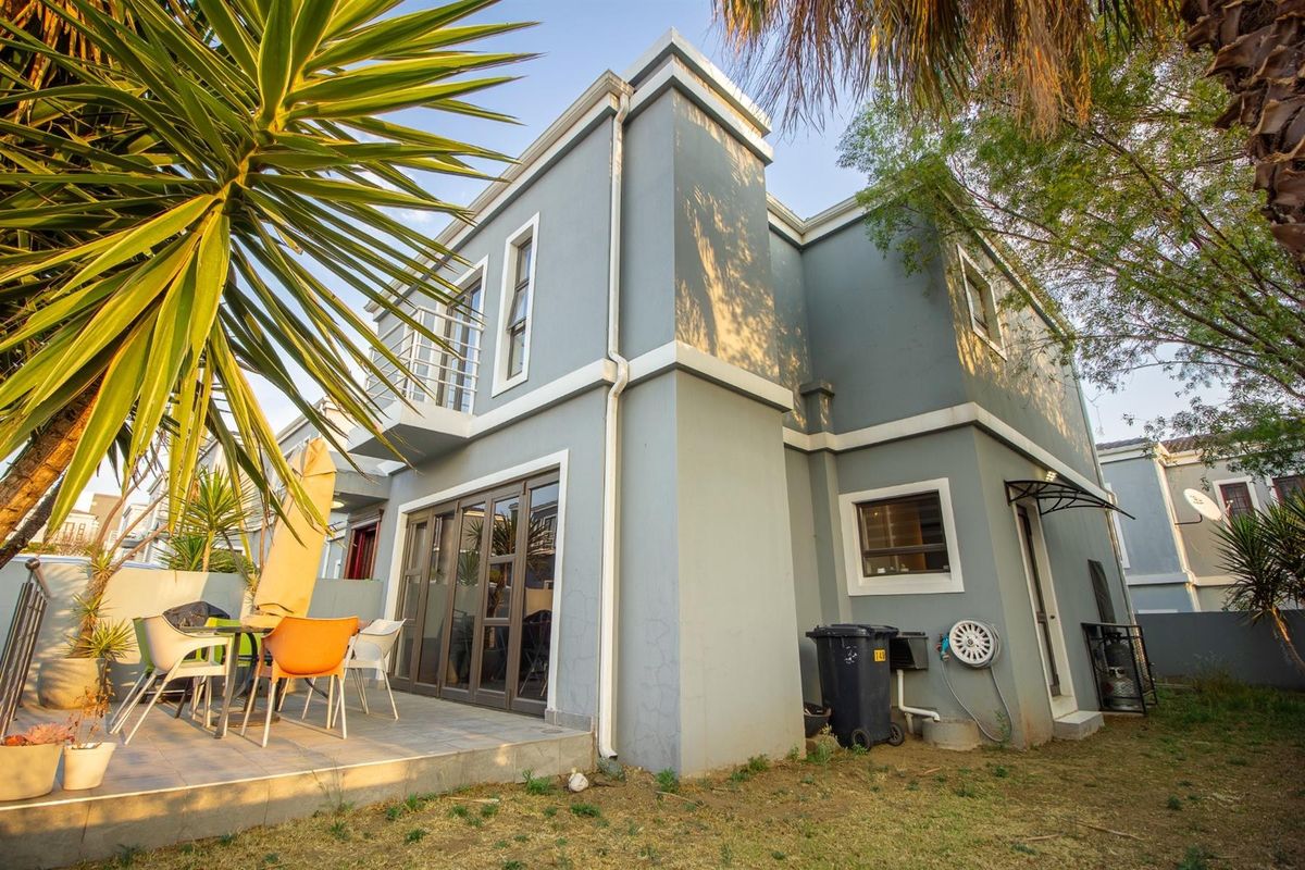 Rear view of a double-storey house featuring a tiled patio, aluminium sliding doors, and a small balcony, set within a private garden area.