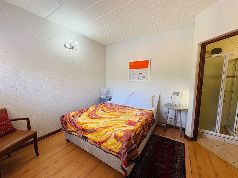 A functional bedroom featuring laminate flooring, textured walls, and an attached en-suite shower room.