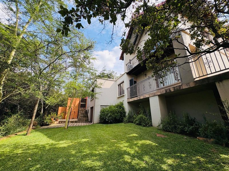 Rear view of the property featuring a multi-level exterior with balconies, wrought iron railings, a paved patio area, and a well-maintained garden.