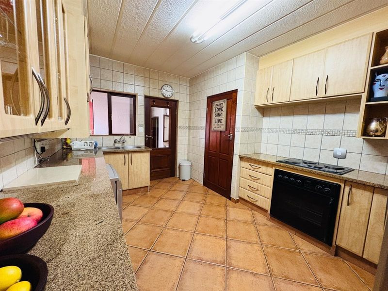 A functional kitchen featuring granite countertops, built-in oven, electric hob, tiled backsplash, and ample wooden cabinetry with tiled flooring.
