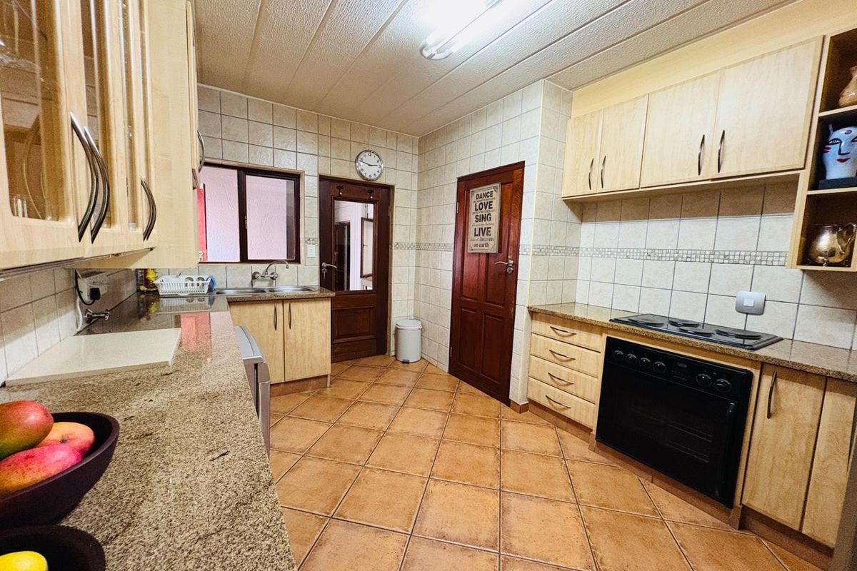 A functional kitchen featuring granite countertops, built-in oven, electric hob, tiled backsplash, and ample wooden cabinetry with tiled flooring.