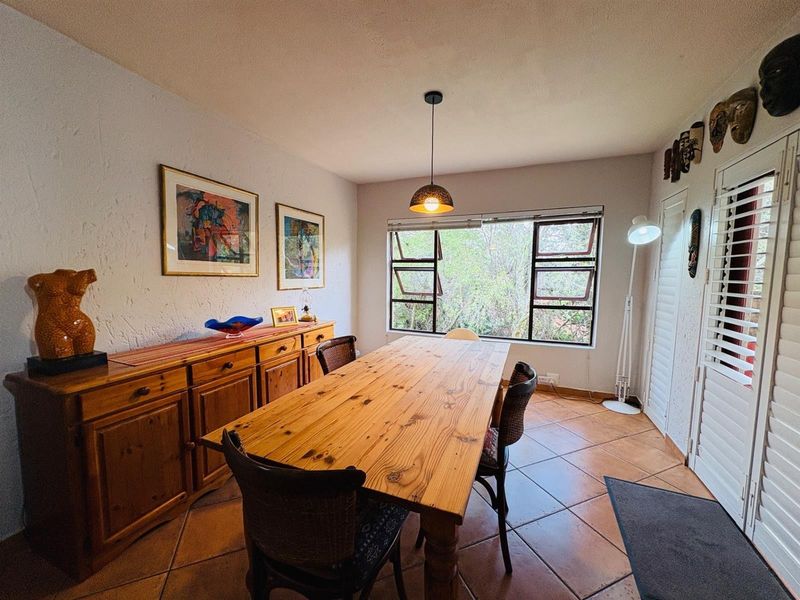 A dining room featuring terracotta floor tiles, a pendant light, and large top-hung windows overlooking the garden.