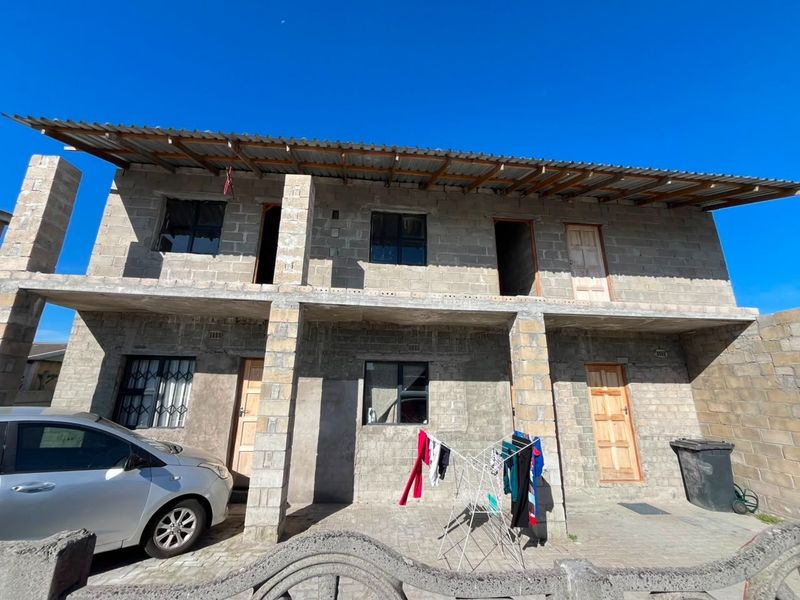 Two-story residential building featuring unfinished concrete block construction, a corrugated metal roof, and a paved ground-level entrance area.