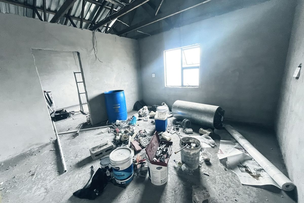 An unfinished bedroom space featuring exposed roof trusses, cement screed flooring, and plastered walls, currently in a shell condition awaiting final finishes.