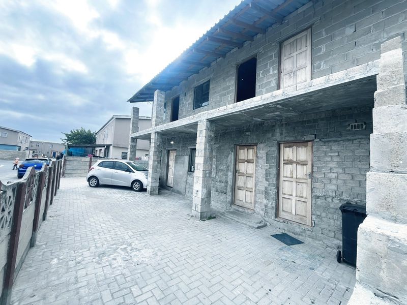Two-story residential building featuring unfinished concrete block construction, multiple timber entry doors, and a paved driveway area.